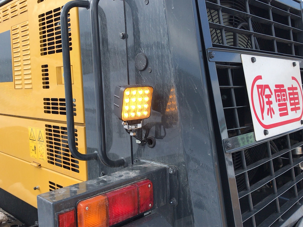 除雪グレーダー（GD675）のサイドに設置された48WイエローLED作業灯。吹雪や濃霧でも光が散乱しにくい黄色光で視認性を確保。