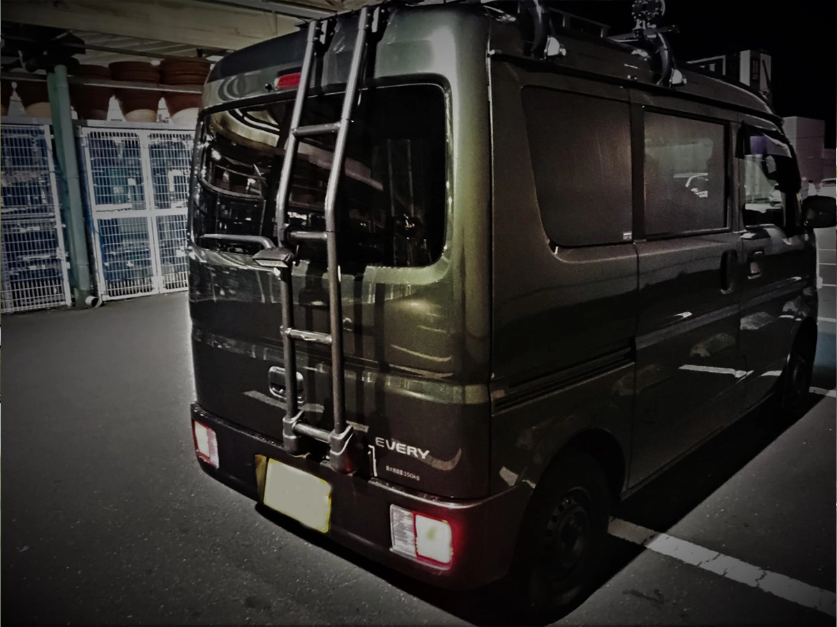 スズキ・エブリイのフロントバンパーガード（パイプ）に、専用ブラケットで設置された18W LED作業灯。穴あけ加工なしで後方の照射範囲を補完する設置事例。