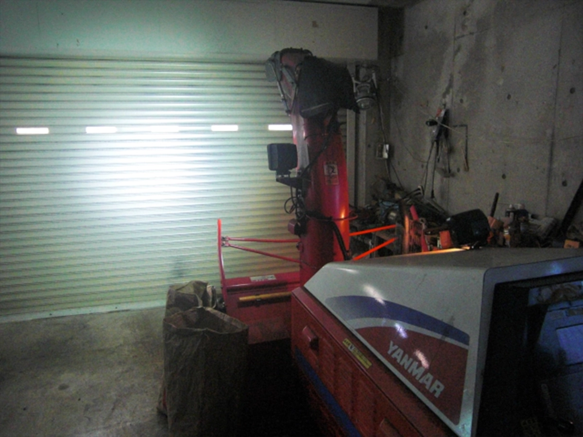 夜間の倉庫で、シャッターに向けて点灯するヤンマー除雪機のLED作業灯（投雪口設置）。